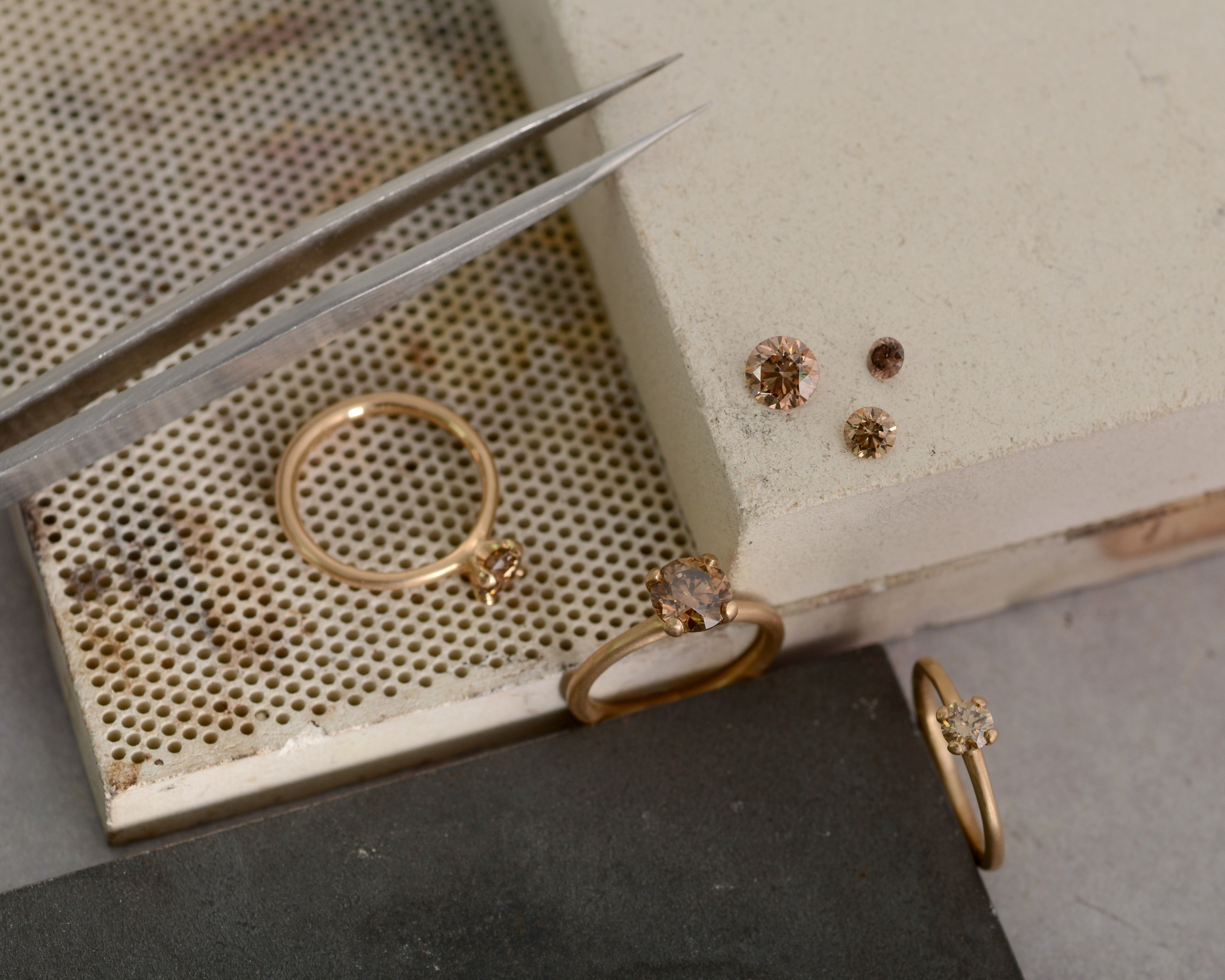 Gold rings with champagne cognac diamonds on a textured surface with tweezers